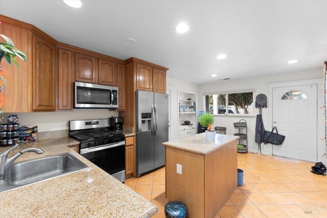 kitchen featuring light stone countertops, sink, light tile patterned flooring, a kitchen island, and appliances with stainless steel finishes