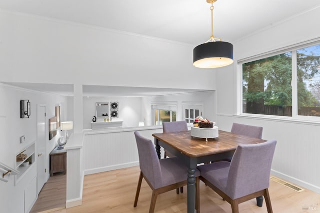 dining space with ornamental molding and light hardwood / wood-style flooring