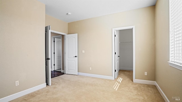 unfurnished bedroom featuring a walk in closet, light colored carpet, and a closet