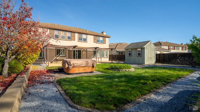 back of property featuring a yard, a hot tub, and an outdoor structure