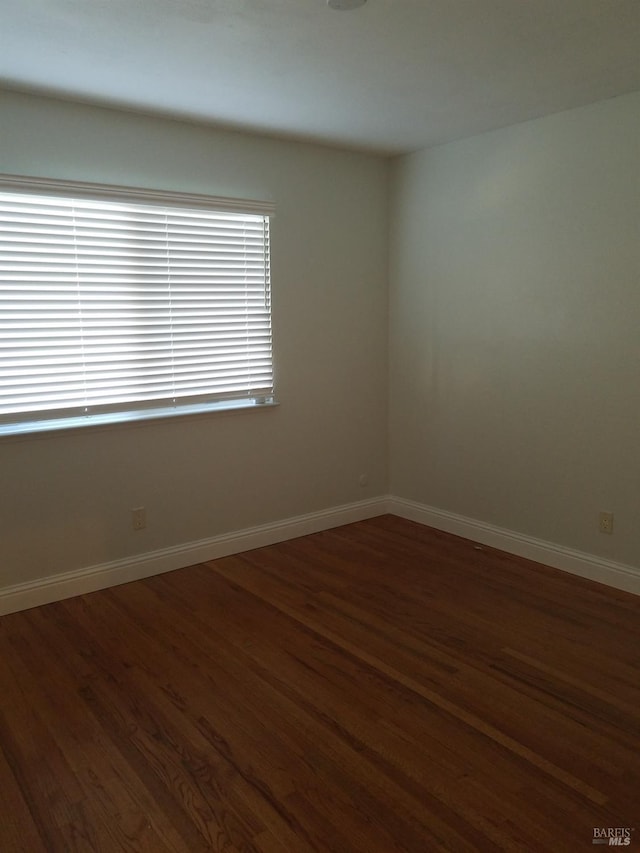 spare room featuring baseboards and dark wood finished floors