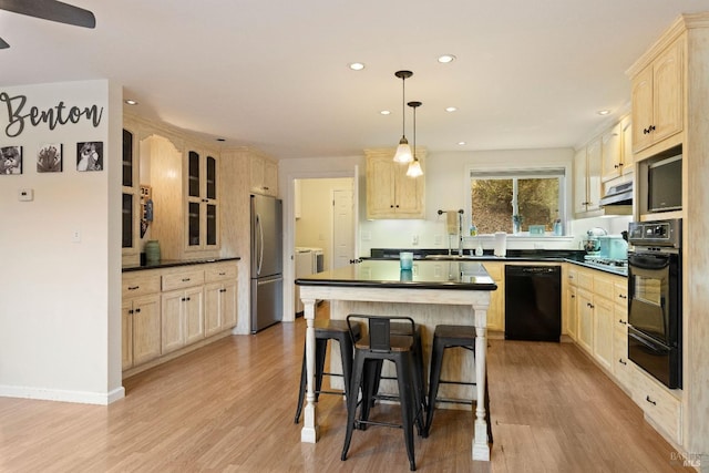 kitchen with pendant lighting, black appliances, sink, a kitchen island, and light hardwood / wood-style floors