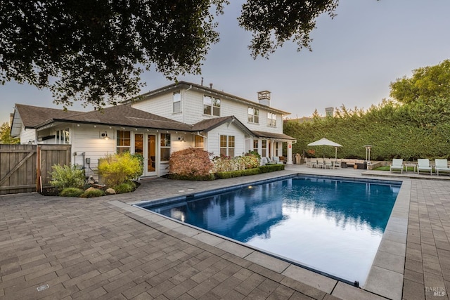 back house at dusk featuring a patio area and a fenced in pool