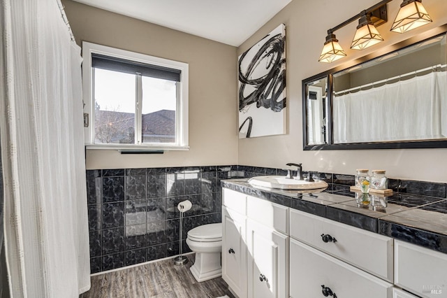 bathroom with toilet, a wainscoted wall, wood finished floors, vanity, and tile walls