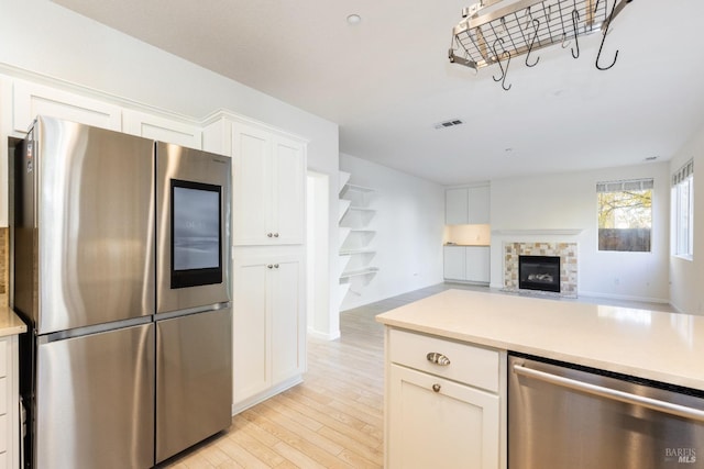 kitchen with a tiled fireplace, white cabinets, stainless steel appliances, and light wood-type flooring