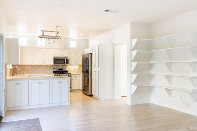 kitchen featuring backsplash, sink, light wood-type flooring, white cabinetry, and stainless steel appliances