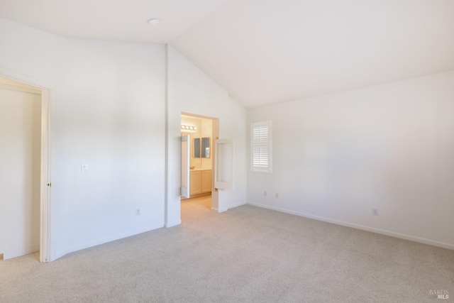 unfurnished bedroom with ensuite bathroom, light colored carpet, and lofted ceiling