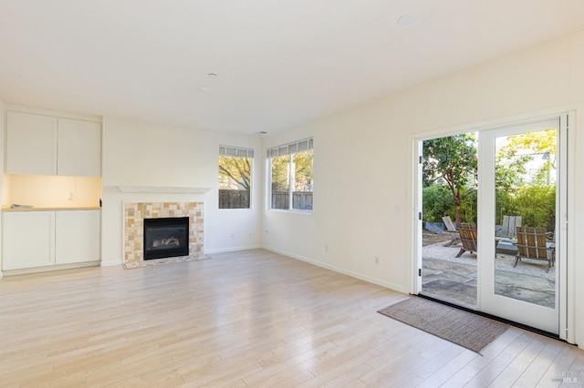 unfurnished living room featuring plenty of natural light, light hardwood / wood-style floors, and a tiled fireplace