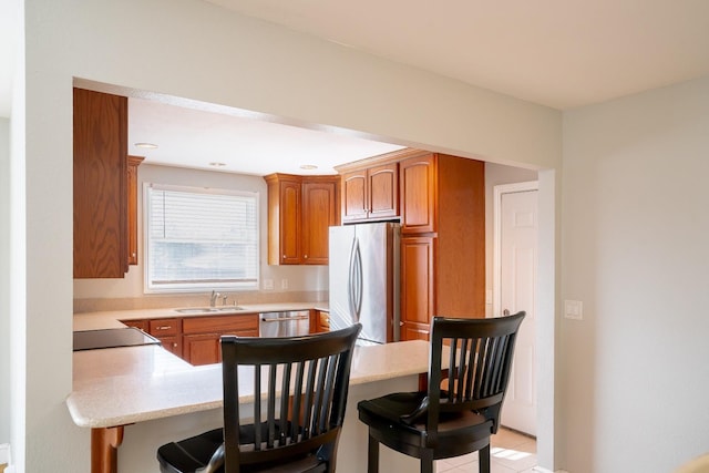 kitchen with sink, light tile patterned floors, a breakfast bar, appliances with stainless steel finishes, and kitchen peninsula