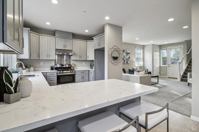 kitchen with sink, stainless steel gas range, gray cabinets, light colored carpet, and kitchen peninsula