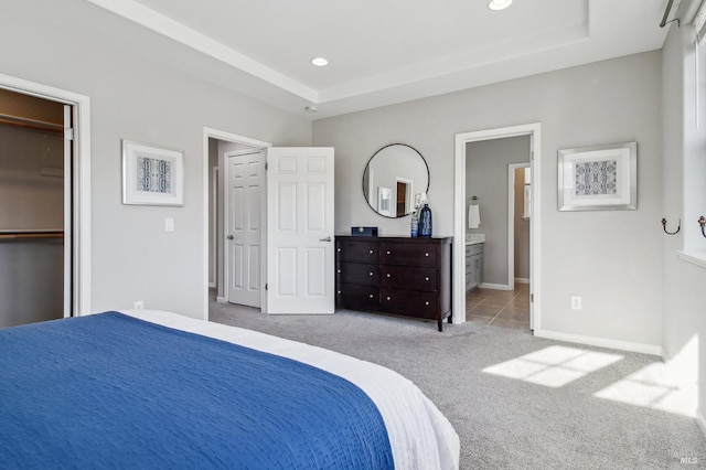 bedroom with a tray ceiling, connected bathroom, and light carpet