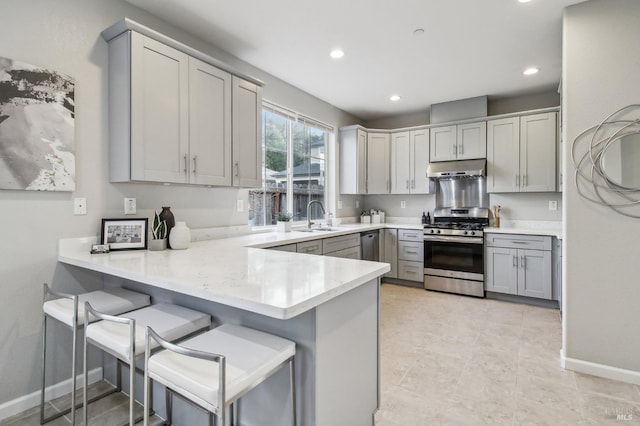 kitchen with kitchen peninsula, stainless steel gas range oven, gray cabinetry, and a breakfast bar area