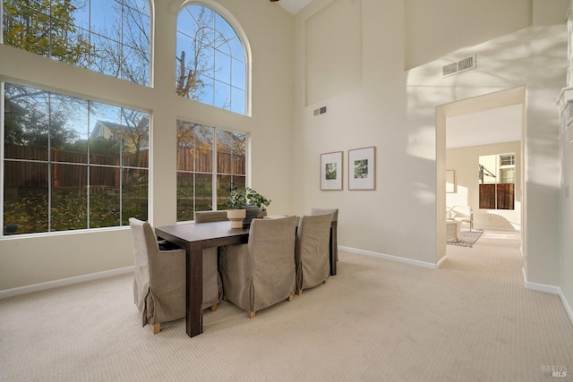 dining space featuring a towering ceiling, visible vents, light carpet, and baseboards