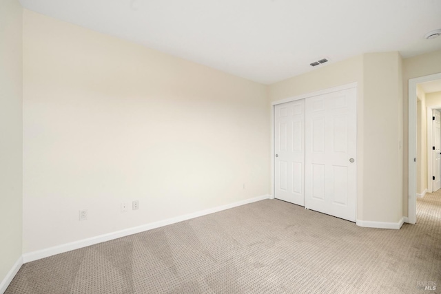 unfurnished bedroom with a closet, light colored carpet, visible vents, and baseboards