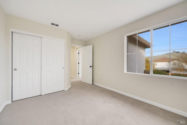 unfurnished bedroom with baseboards, visible vents, a closet, and light colored carpet