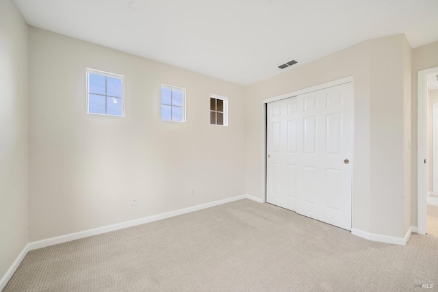 unfurnished bedroom with a closet, light carpet, visible vents, and baseboards