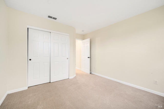 unfurnished bedroom featuring a closet, light colored carpet, visible vents, and baseboards