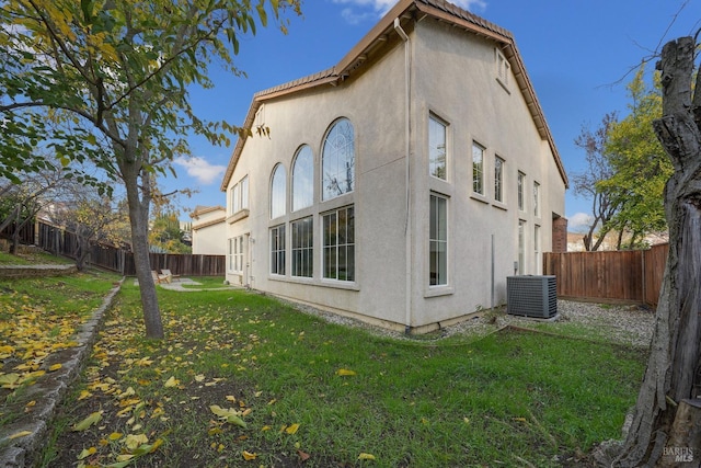 view of side of home featuring stucco siding, a fenced backyard, a lawn, and central AC unit