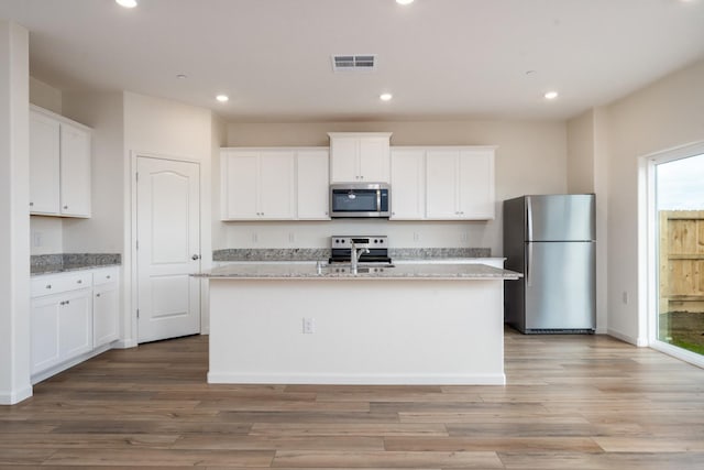 kitchen featuring white cabinets, appliances with stainless steel finishes, light wood-type flooring, and an island with sink