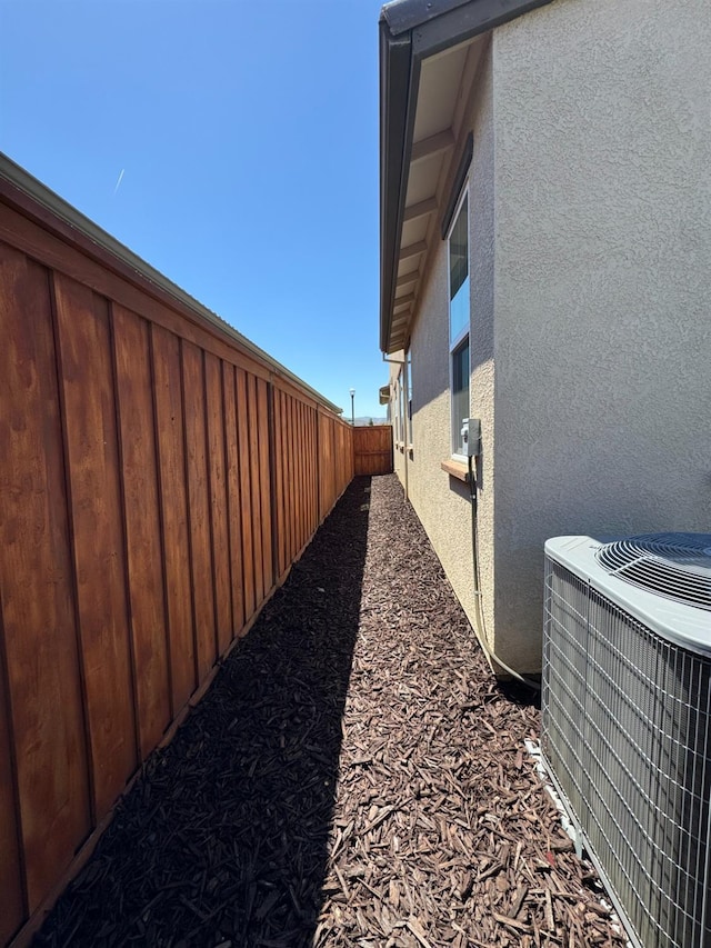 view of side of property featuring a fenced backyard, central AC, and stucco siding