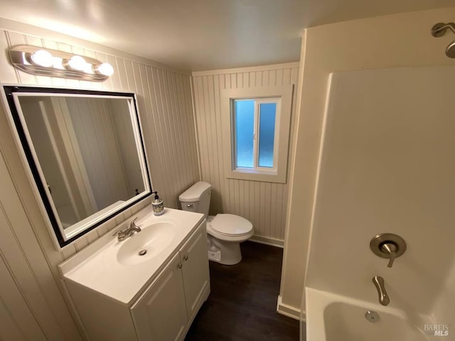 full bathroom featuring wood walls, hardwood / wood-style floors, toilet, vanity, and shower / bathtub combination