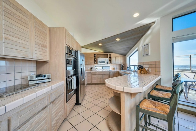 kitchen with appliances with stainless steel finishes, tasteful backsplash, light brown cabinets, light tile patterned floors, and tile counters