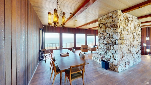 dining space with a water view, wood-type flooring, a chandelier, wooden walls, and beam ceiling