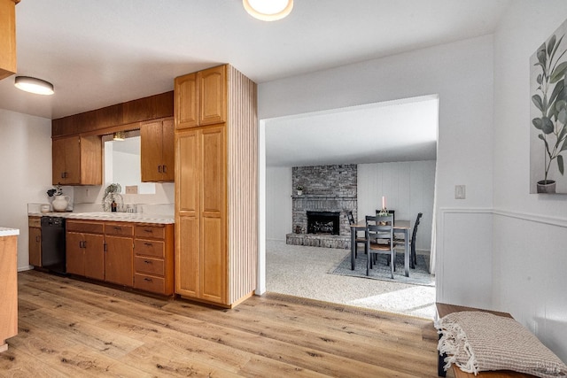 kitchen with dishwasher, a large fireplace, sink, and light hardwood / wood-style floors