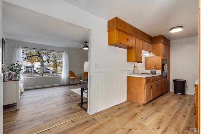 kitchen with stainless steel gas cooktop, black oven, ceiling fan, and light hardwood / wood-style flooring