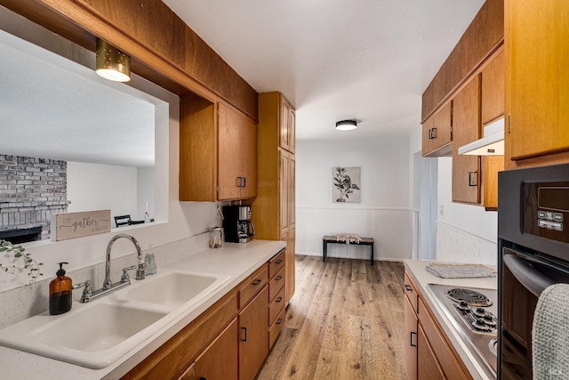 kitchen with sink, black oven, light hardwood / wood-style flooring, a fireplace, and stainless steel gas stovetop