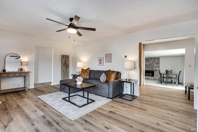 living room with a textured ceiling, light hardwood / wood-style flooring, a large fireplace, and ceiling fan