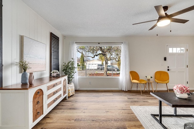 living area with ceiling fan, a textured ceiling, and light hardwood / wood-style flooring