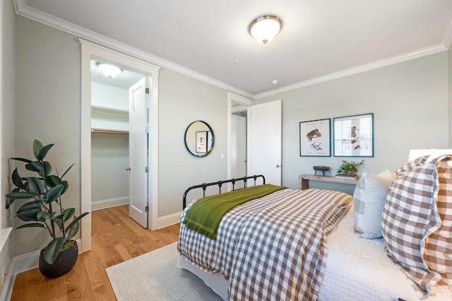 bedroom with a spacious closet, ornamental molding, light hardwood / wood-style floors, and a closet