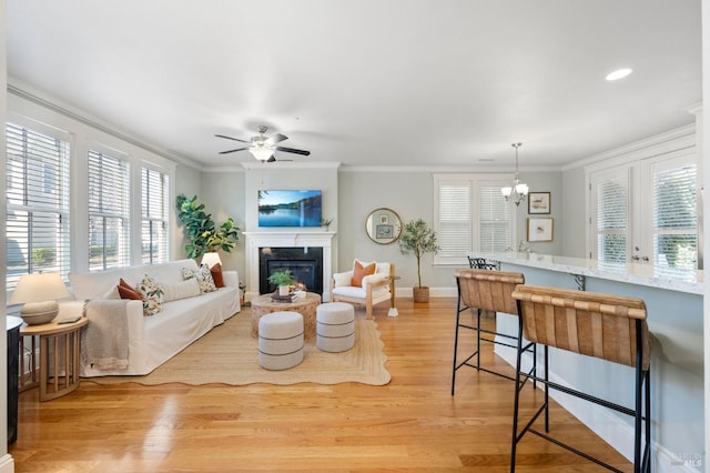 living room with crown molding, ceiling fan with notable chandelier, and light hardwood / wood-style floors