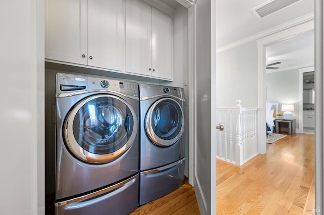 laundry area featuring crown molding, washer and clothes dryer, light hardwood / wood-style floors, and cabinets