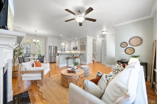 living room with ornamental molding, ceiling fan with notable chandelier, and light hardwood / wood-style floors