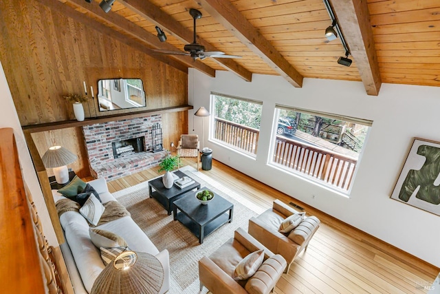 living room with rail lighting, ceiling fan, lofted ceiling with beams, a fireplace, and hardwood / wood-style floors