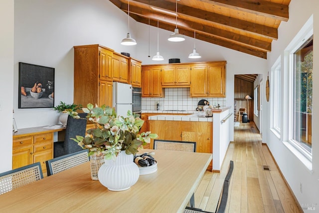 kitchen with tile countertops, decorative backsplash, oven, light wood-style floors, and beam ceiling