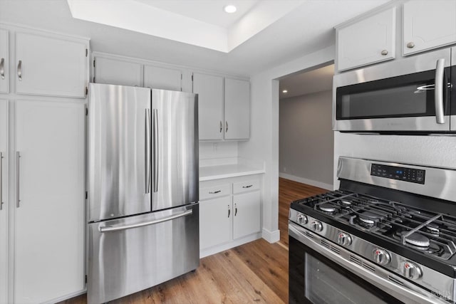 kitchen with baseboards, light wood-style flooring, stainless steel appliances, white cabinetry, and a raised ceiling
