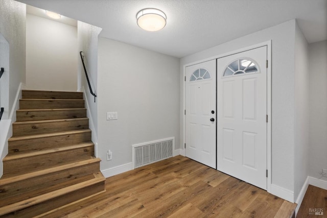 entryway with stairs, wood finished floors, visible vents, and baseboards