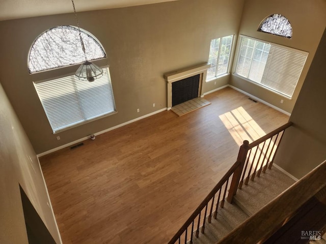 unfurnished living room with a tile fireplace, hardwood / wood-style floors, high vaulted ceiling, and a chandelier