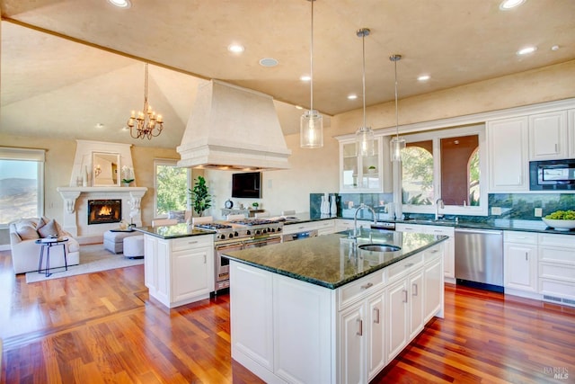 kitchen with a center island with sink, open floor plan, custom exhaust hood, stainless steel appliances, and a sink