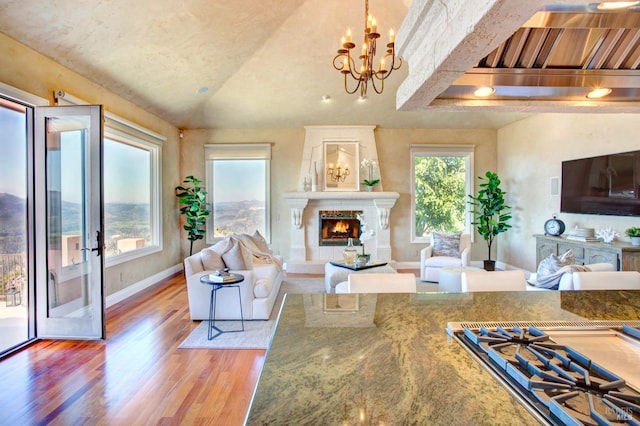 living area with a notable chandelier, a premium fireplace, light wood-style floors, vaulted ceiling, and baseboards