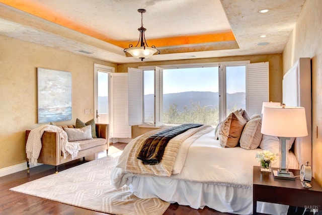 bedroom featuring a tray ceiling, recessed lighting, a mountain view, wood finished floors, and baseboards