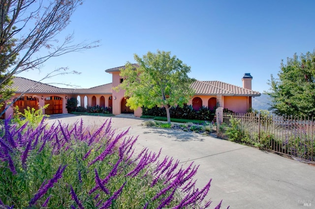 mediterranean / spanish-style house featuring decorative driveway, a chimney, stucco siding, fence, and a tiled roof