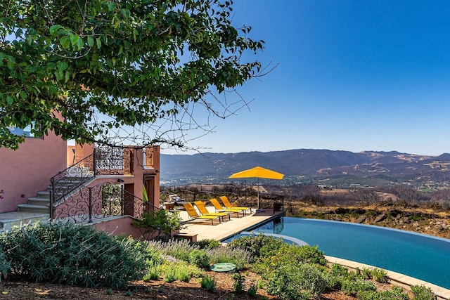 view of pool featuring stairway, an infinity pool, a mountain view, and a patio