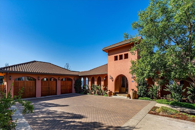 mediterranean / spanish house with a garage, decorative driveway, a tile roof, and stucco siding