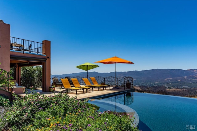 view of swimming pool with an infinity pool, a mountain view, and a patio