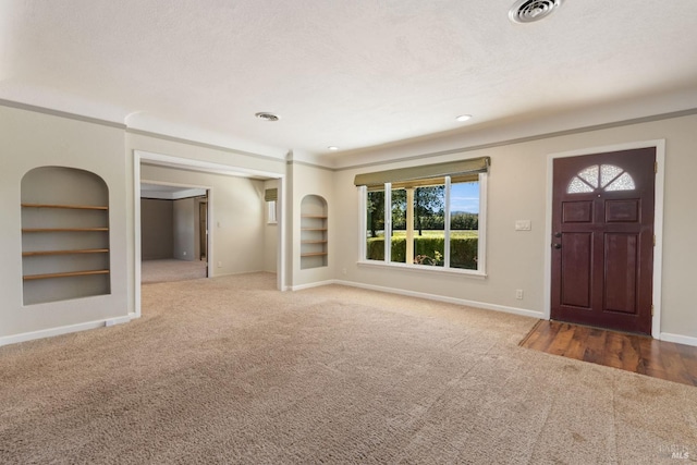 interior space featuring a textured ceiling, carpet floors, built in features, and crown molding