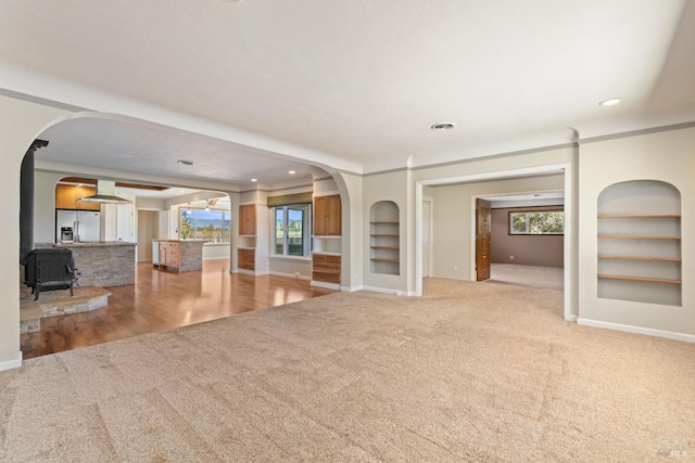 unfurnished living room with built in shelves, a healthy amount of sunlight, and a wood stove